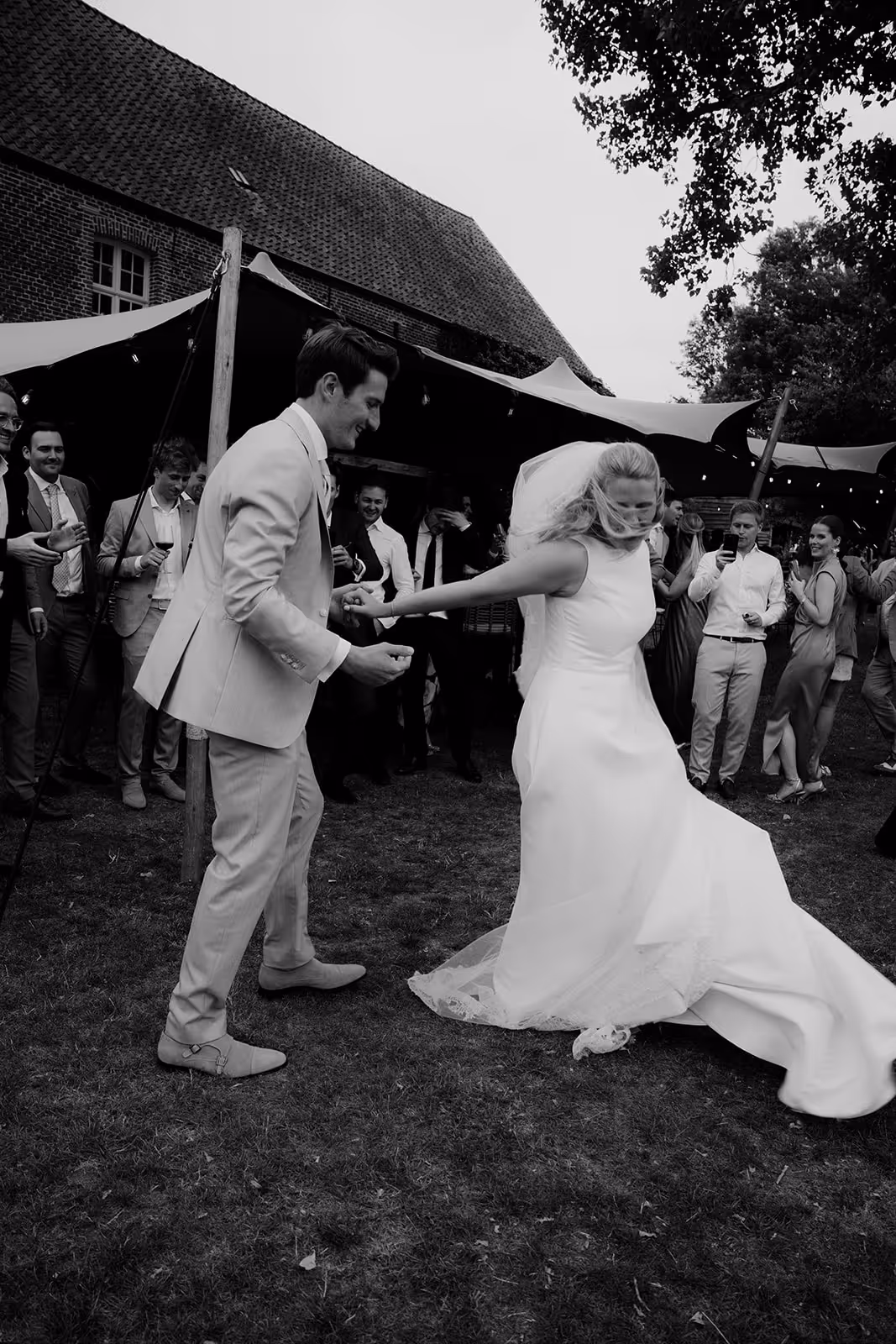 Bride and groom dancing outdoors at a wedding reception with guests watching and photographing them.