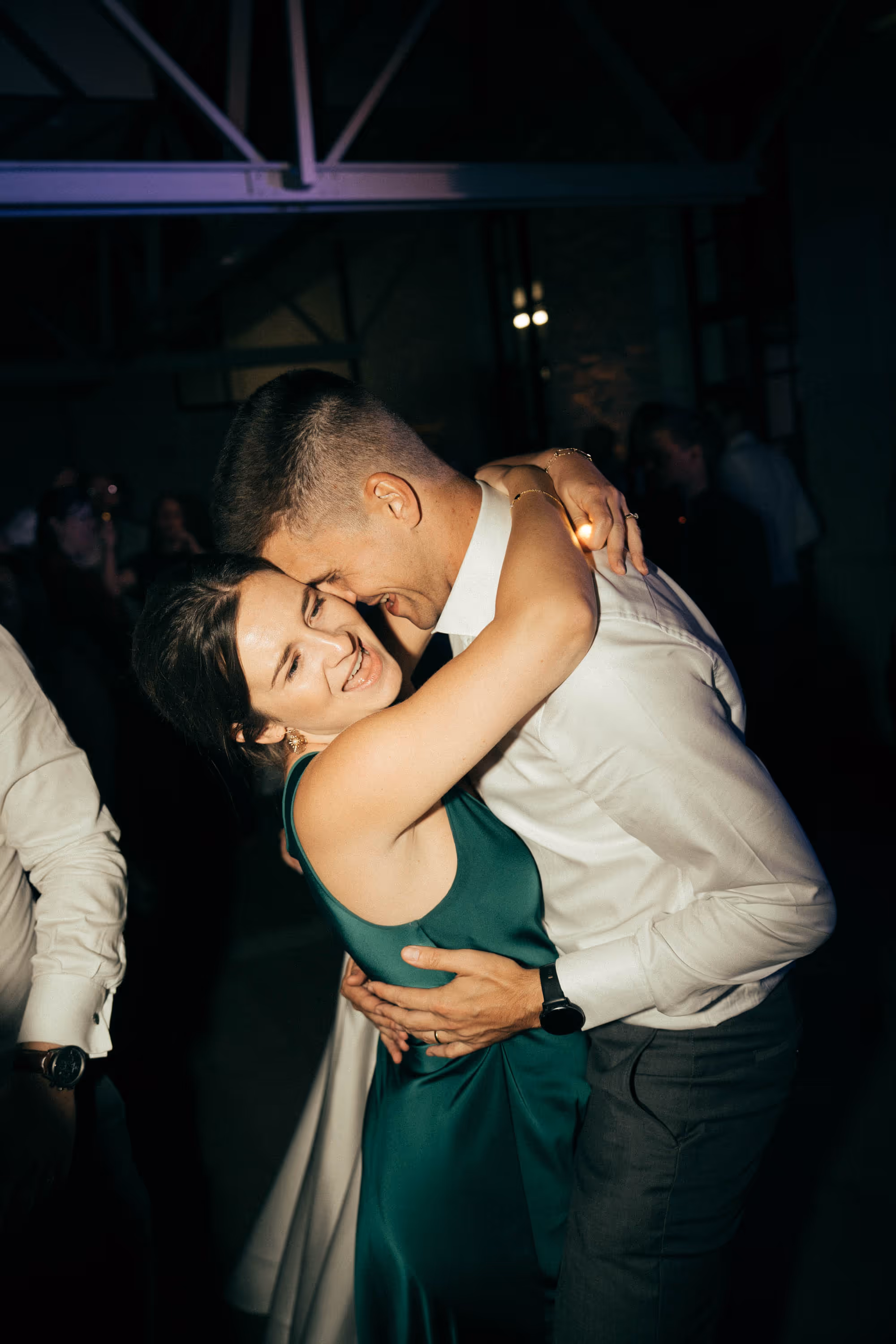 Smiling couple closely embracing each other while dancing at a dimly lit indoor event.