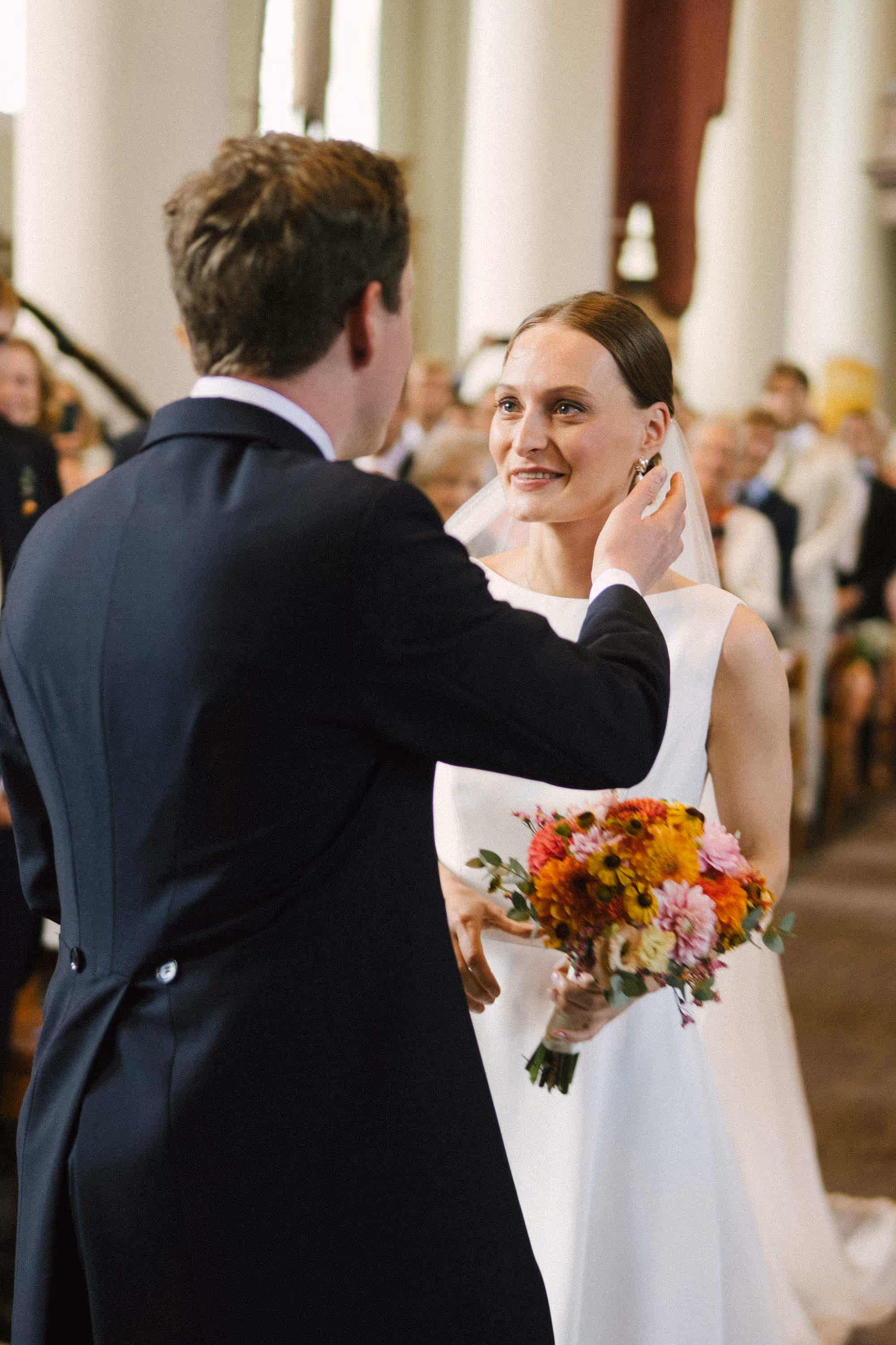 Bride and groom smiling at each other during a wedding ceremony, with the bride holding a colorful flower bouquet.