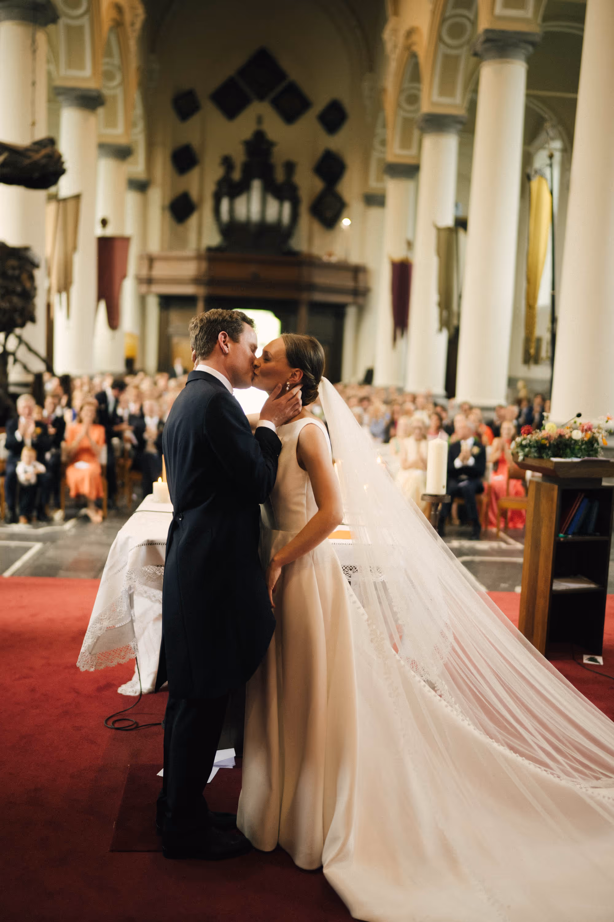 Bride and groom sharing a kiss during their wedding ceremony inside a church with guests seated in the background.