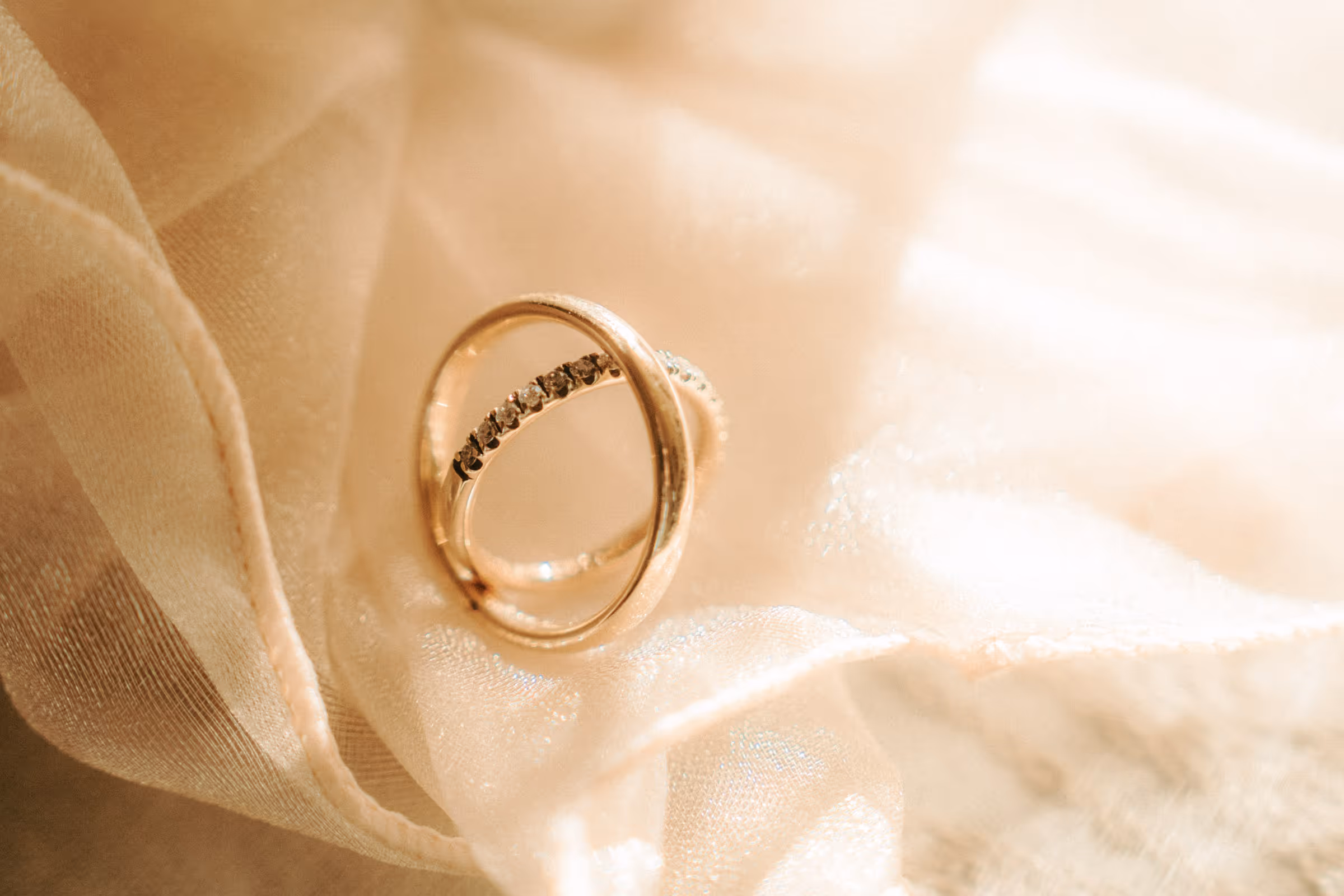 Two gold rings resting on soft beige fabric, one ring is plain and the other has small embedded stones.