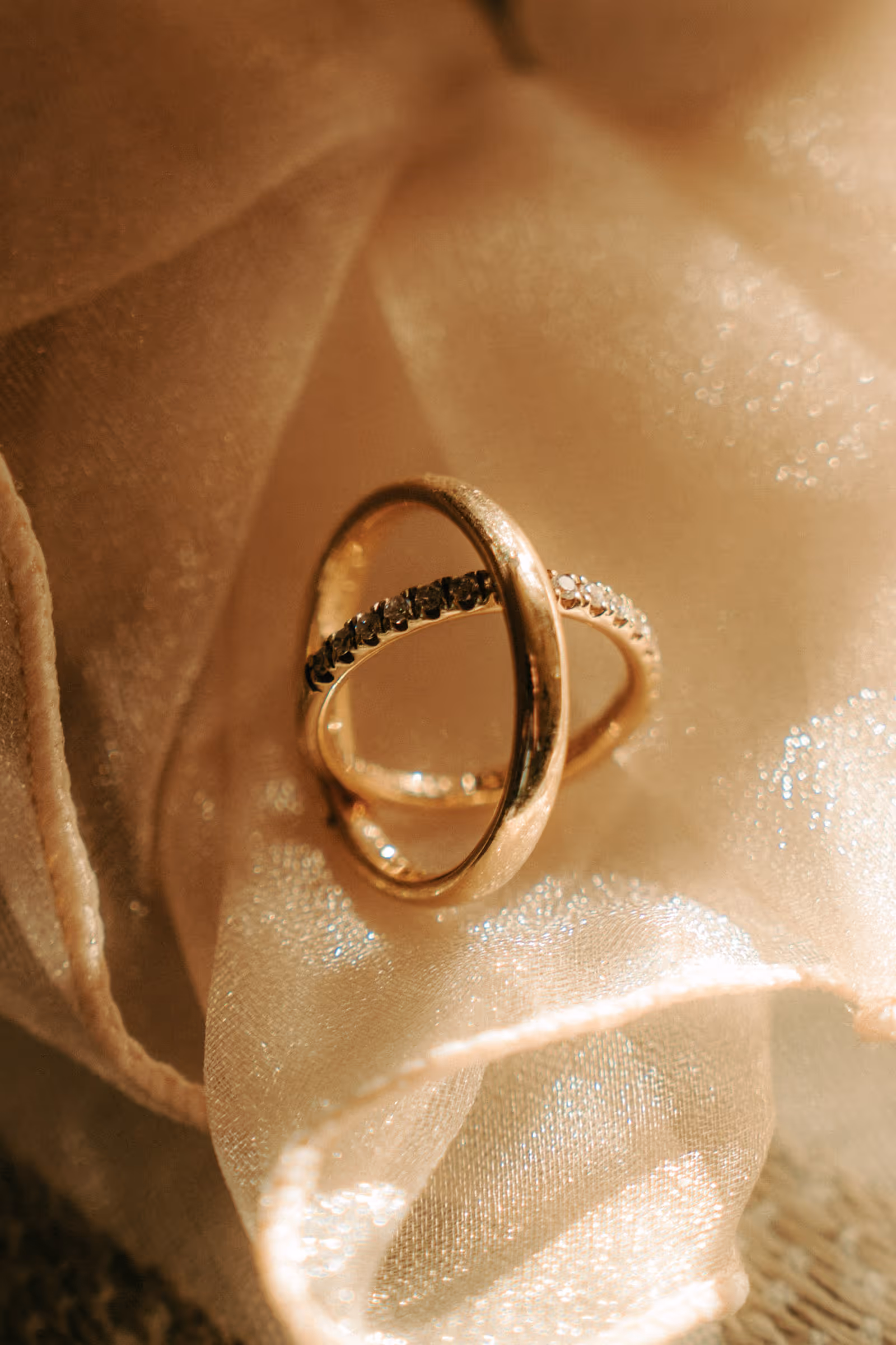 Two gold rings resting on a shimmering beige fabric, one plain band and one with small diamonds.