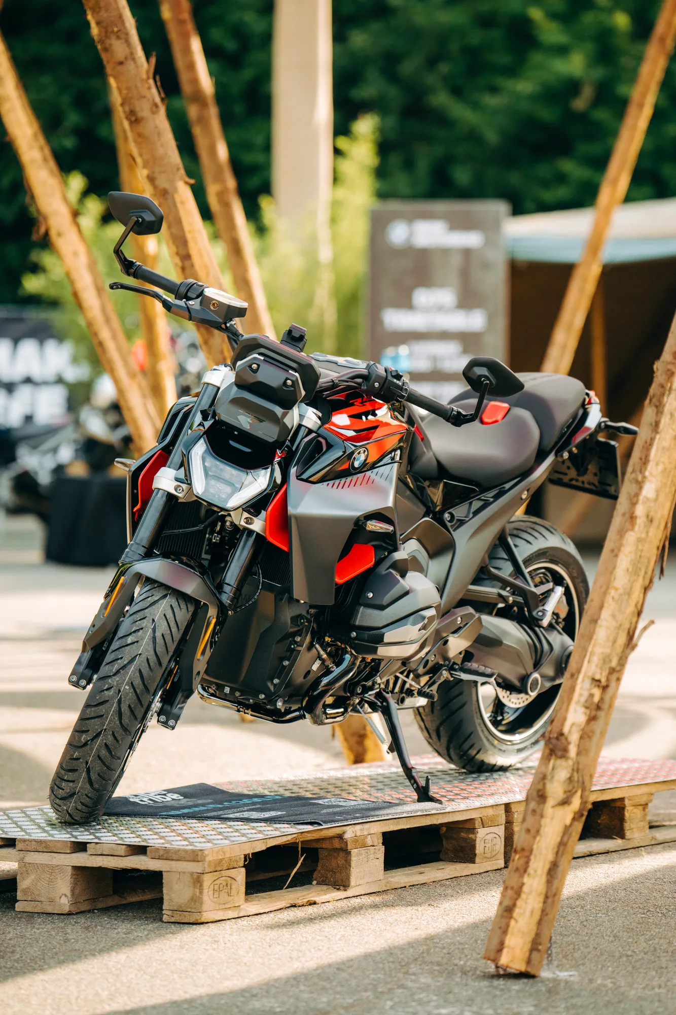 Black and red BMW motorcycle displayed on wooden pallets outdoors with trees in the background.