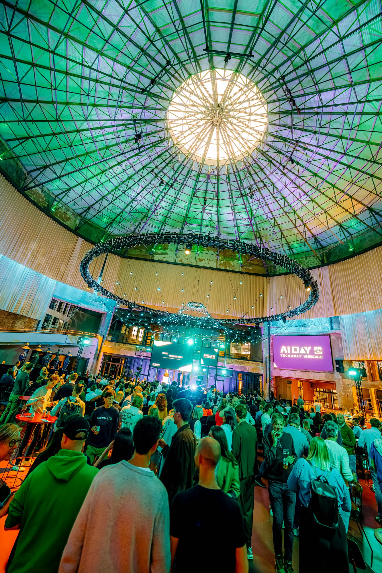 Large crowd gathered inside a venue with a geometric glass dome ceiling and hanging lights for AI Day event.