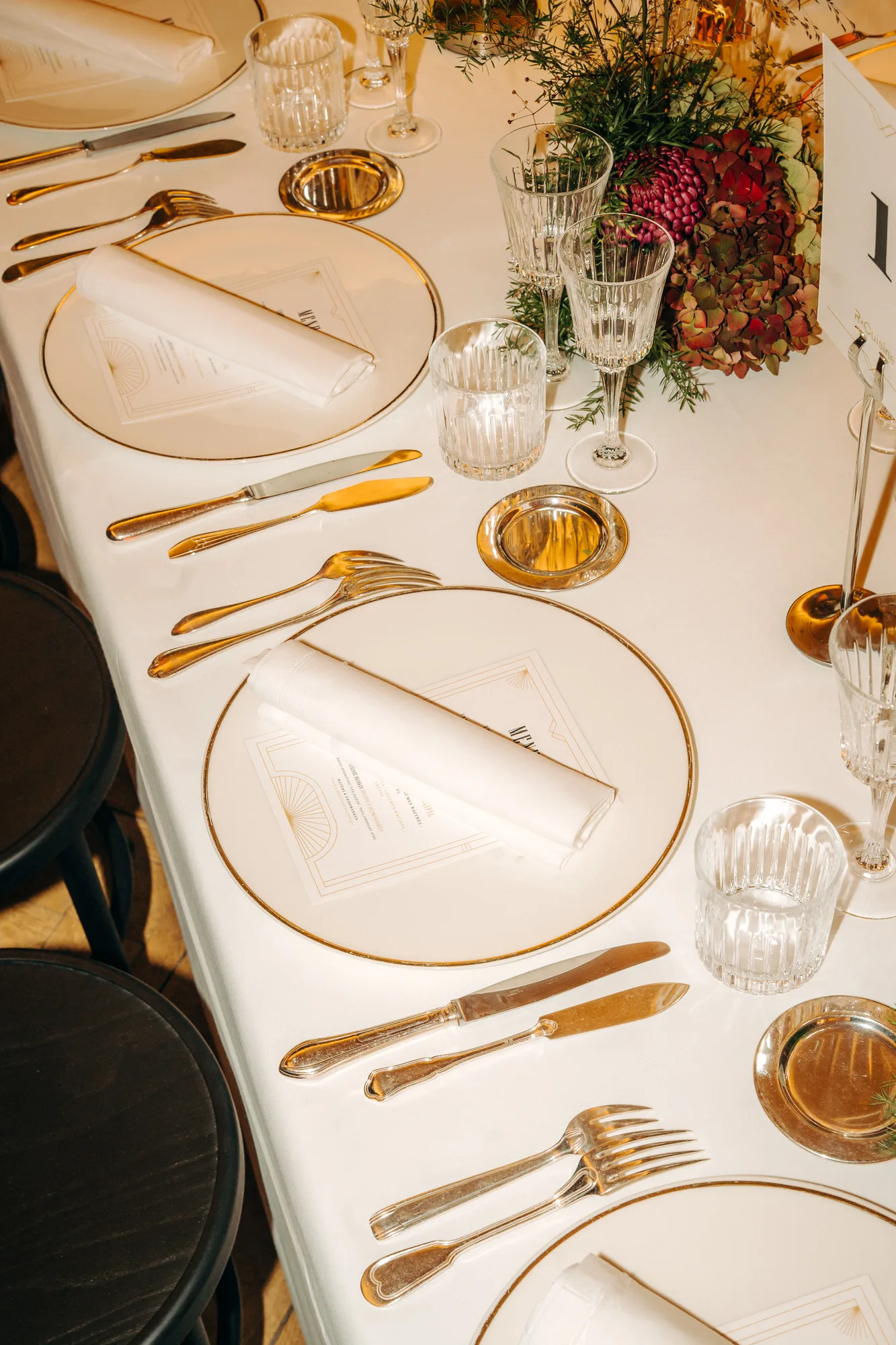 Elegant table setting with white plates, folded napkins, silver cutlery, crystal glasses, and a floral centerpiece on a white tablecloth.