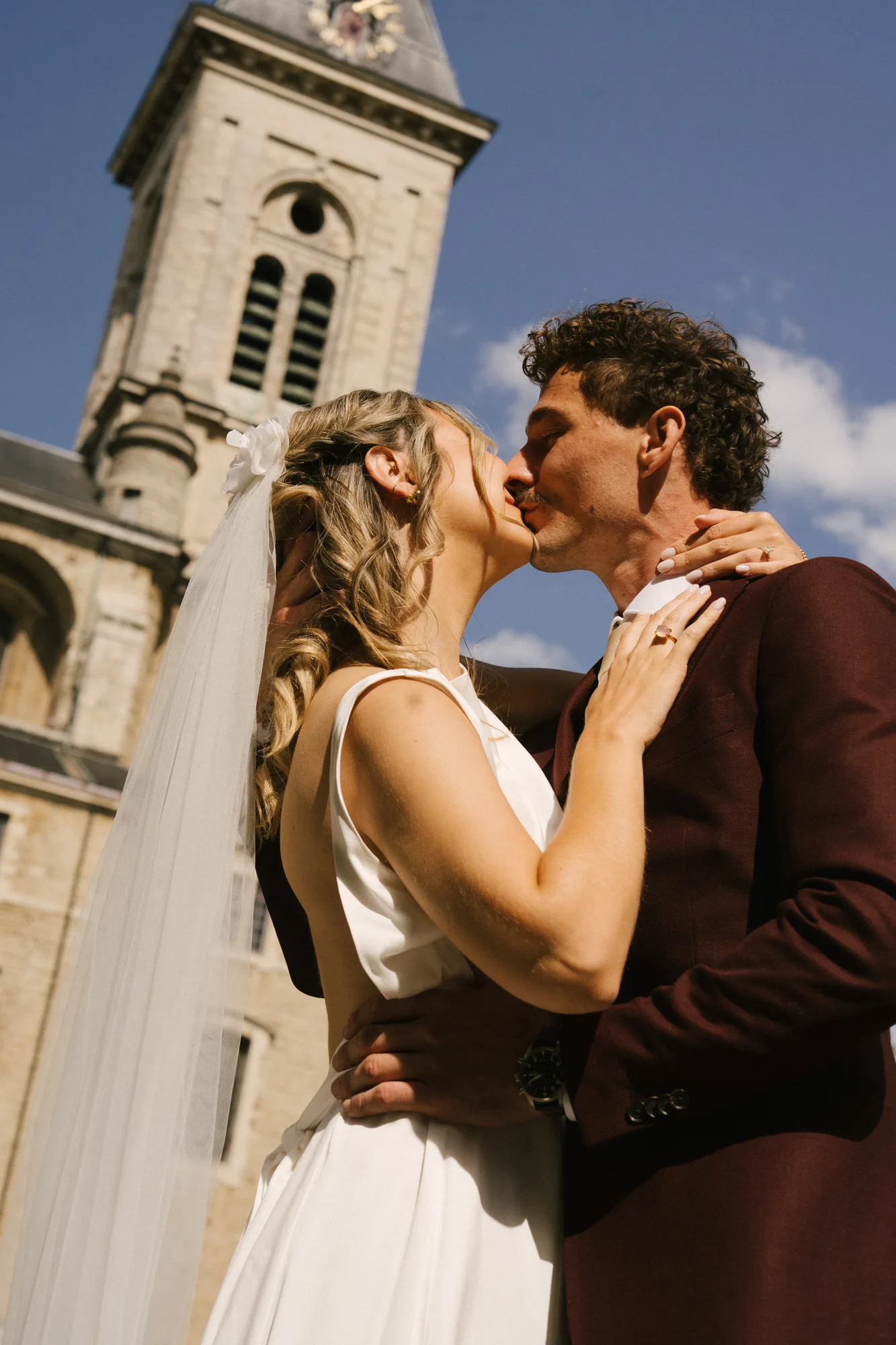 Bride and groom sharing a kiss outdoors with a church tower in the background.