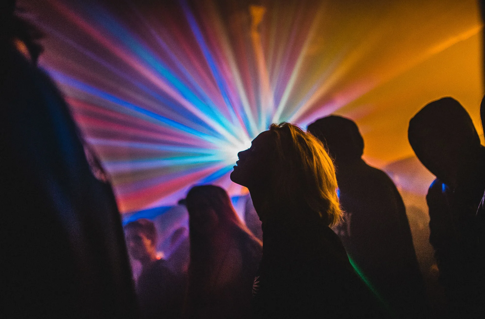 Silhouetted people dancing in a club with colorful radiating lights in the background.