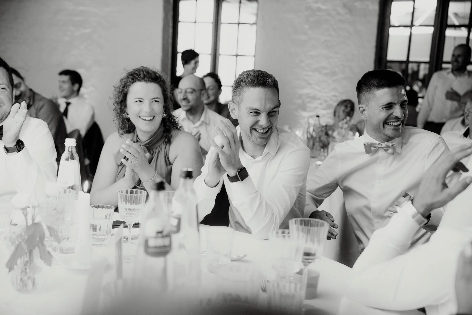 Group of people sitting at a banquet table, clapping and smiling during a celebration.