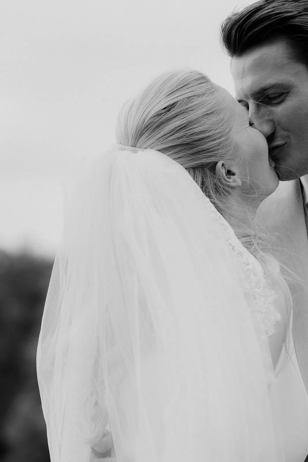 Black and white close-up of a bride and groom sharing a tender kiss, the bride wearing a veil.