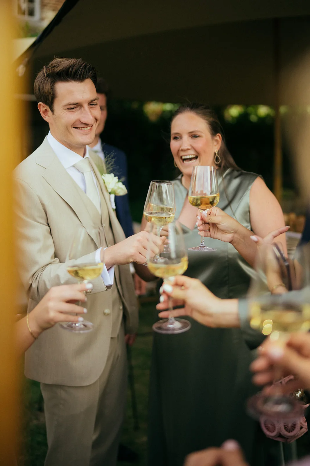 Group of people raising glasses of white wine in a celebratory toast at an outdoor event.