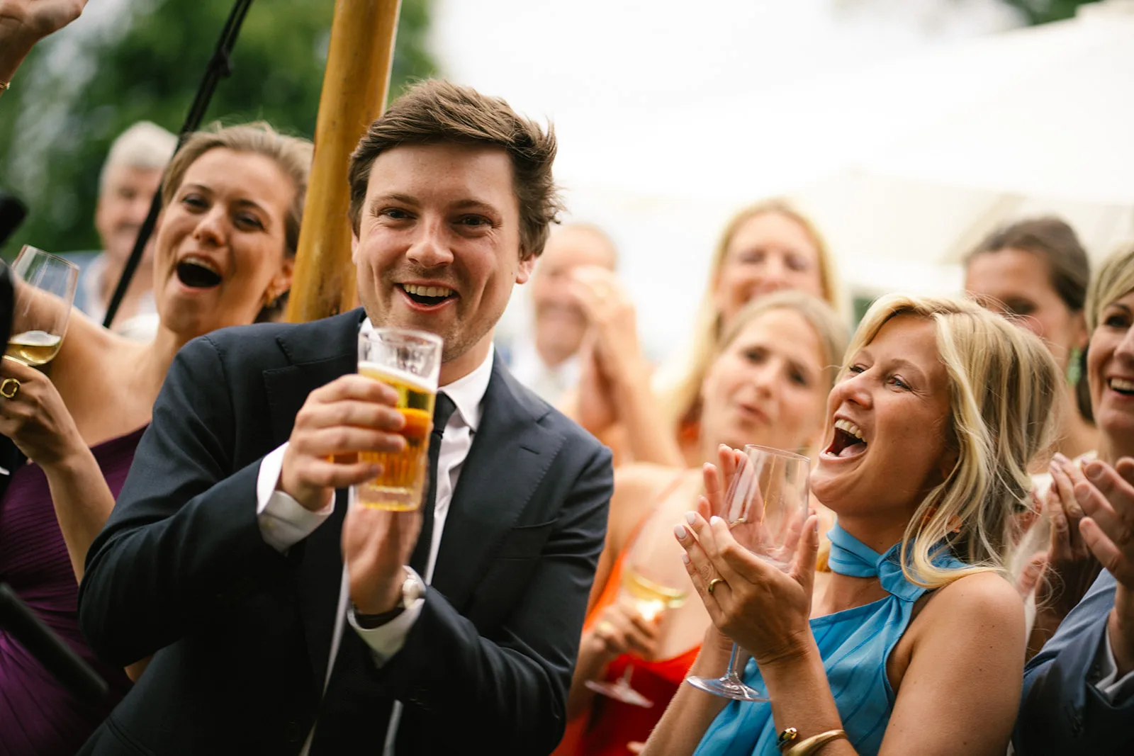 Group of people in formal attire smiling, holding drinks, and celebrating outdoors.