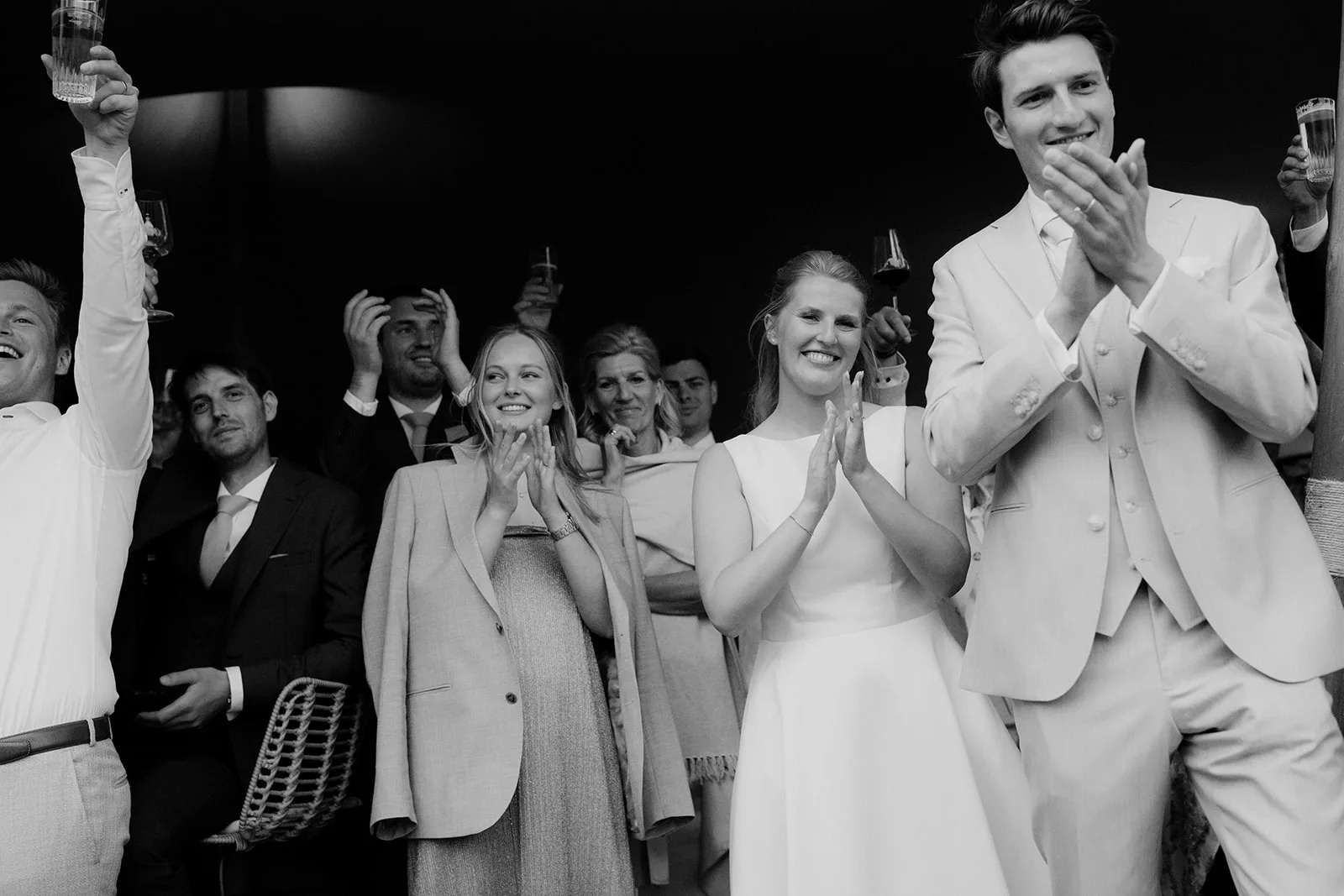 Group of people smiling, clapping, and raising glasses in celebration at a formal event.