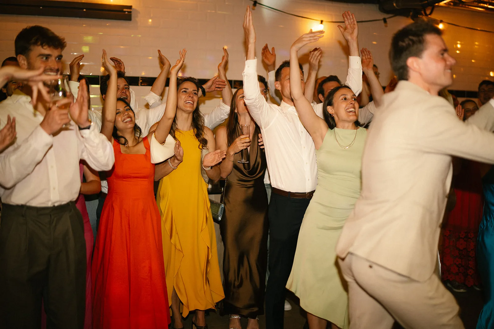 Group of well-dressed people smiling and raising their hands at an indoor celebration.