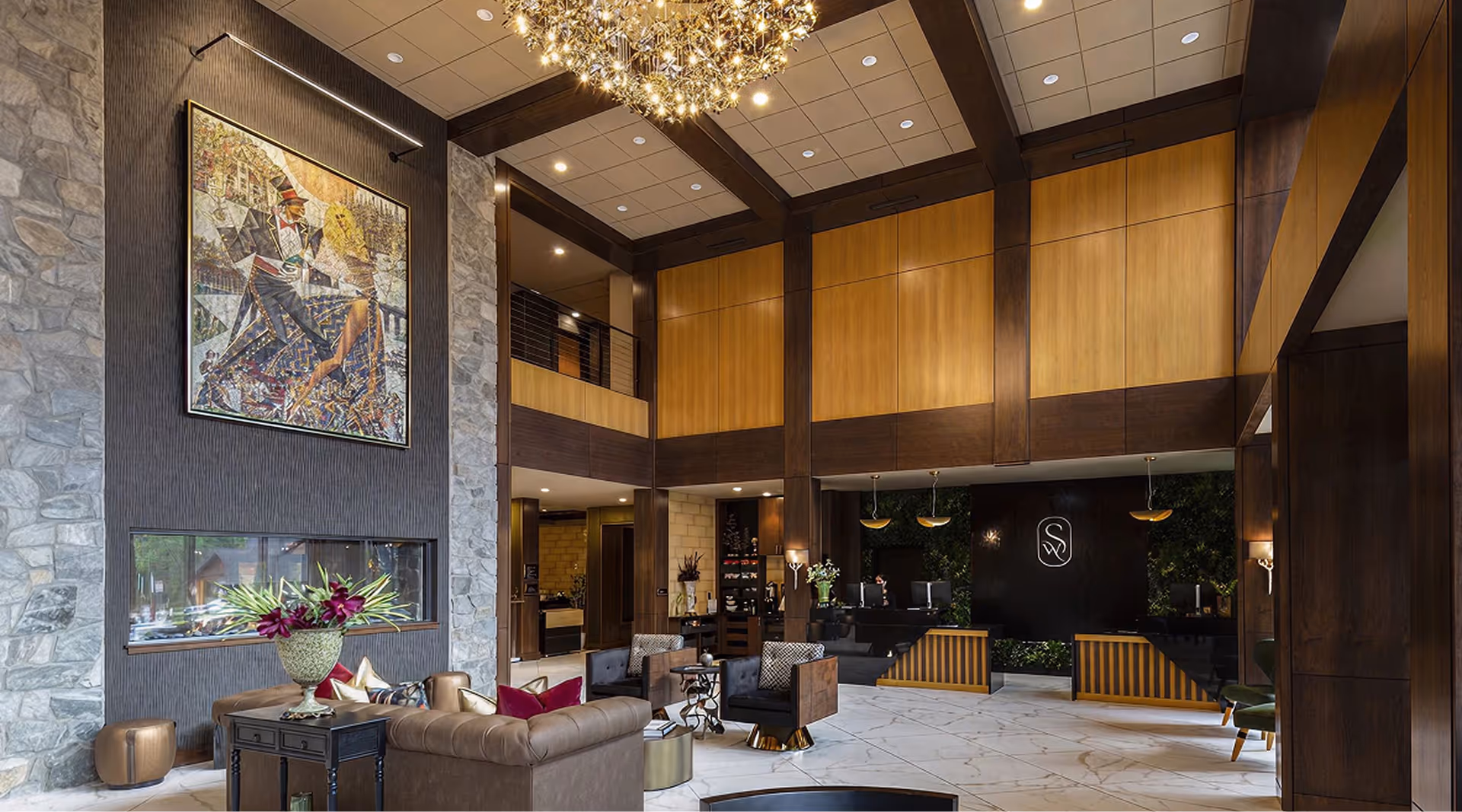Panoramic view of The Swift Water hotel's grand lobby featuring high wood-paneled ceilings, a sparkling chandelier, stone walls, and a modern reception desk.