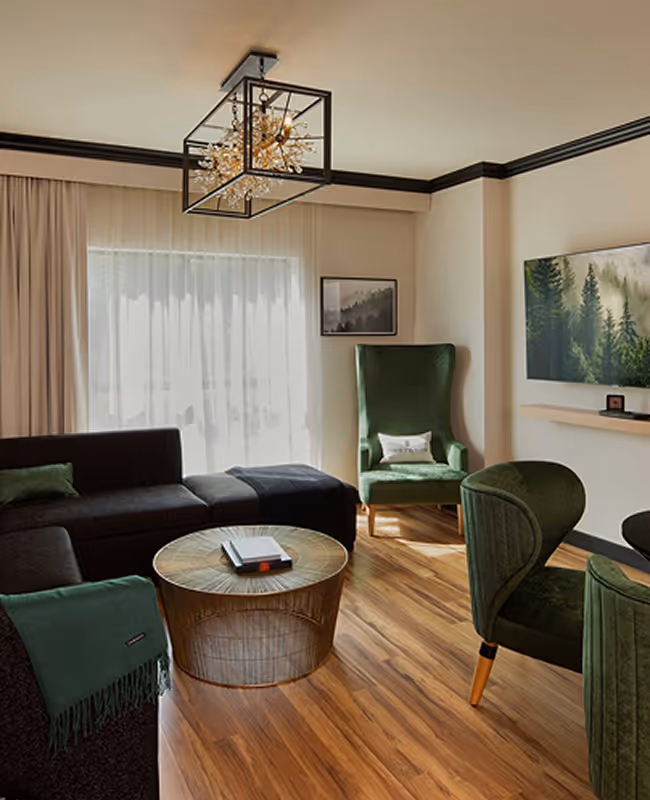 Private living area of a suite at The Swift Water hotel featuring green velvet armchairs, a crystal design light fixture, and natural wood flooring.
