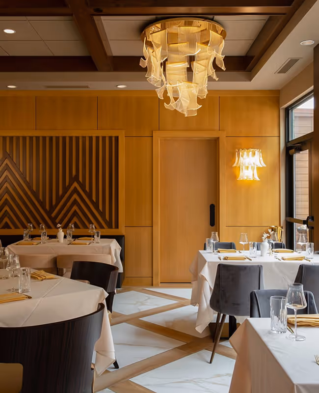 Elegant dining room at The Swift Water hotel featuring white tablecloths, grey velvet chairs, and a sculptural modern glass chandelier.