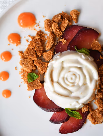Gourmet dessert at The Swift Water hotel featuring a rose-shaped mousse, poached plums, and crunchy crumble.