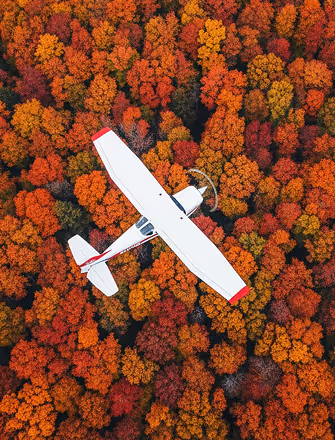 Aerial view of a small white plane flying over a vibrant autumn forest near The Swift Water hotel.