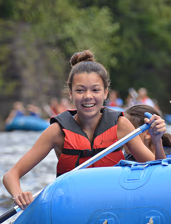 Smiling young girl enjoying white water rafting at The Swift Water hotel, wearing a red life jacket.