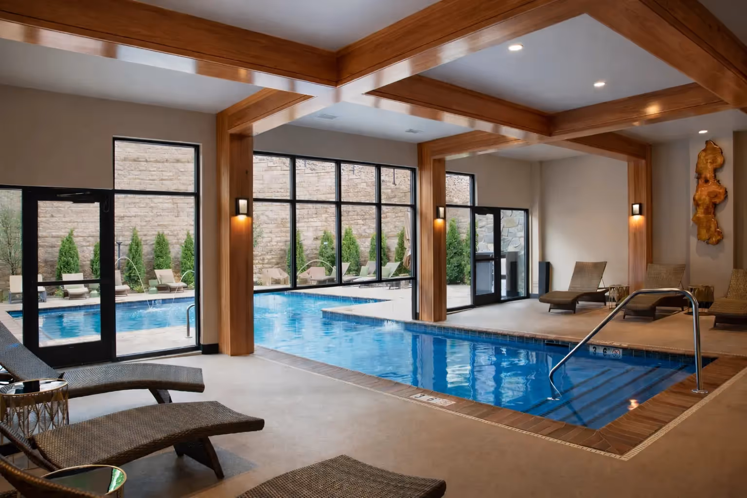 Large indoor heated swimming pool at The Swift Water hotel featuring massive wooden beams, comfortable lounge chairs, and expansive floor-to-ceiling windows.