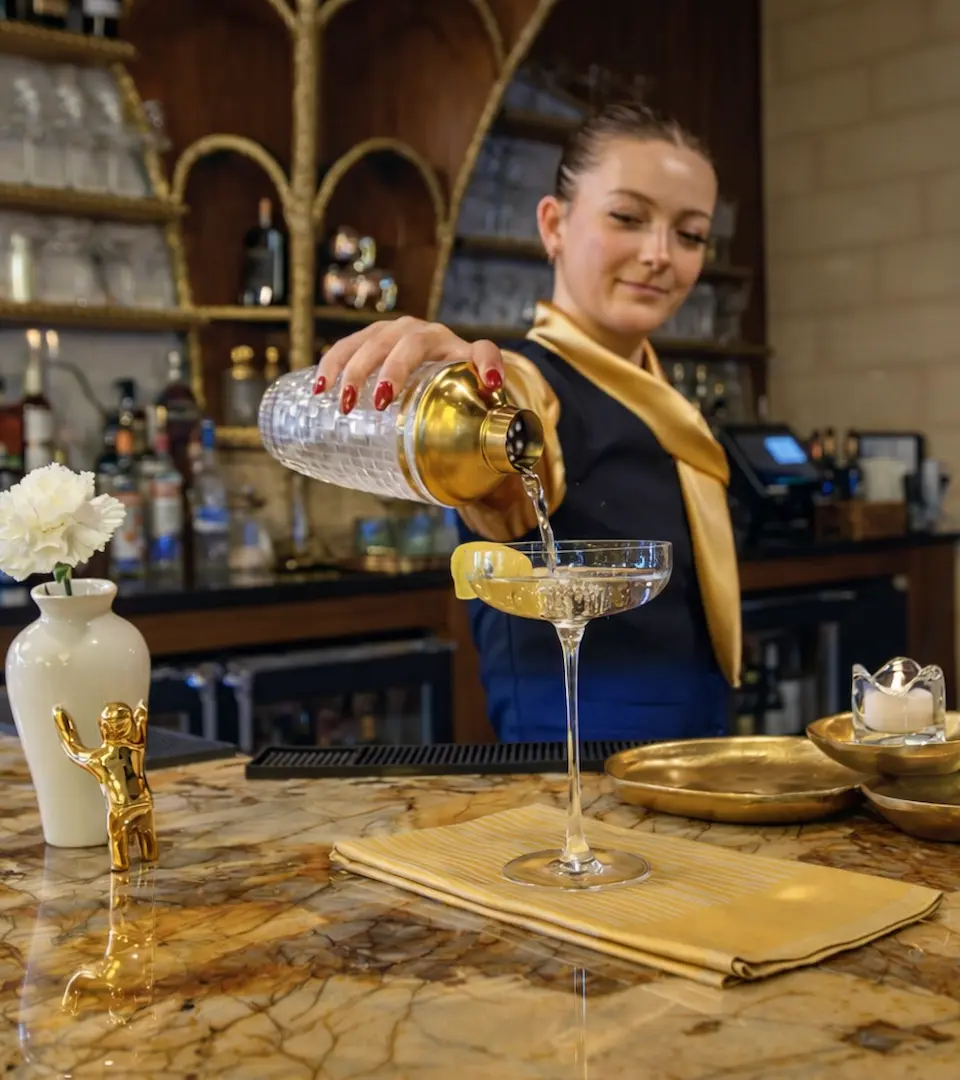 A smiling woman with a straw hat enjoying a wine tasting in a vineyard at The Swift Water hotel.