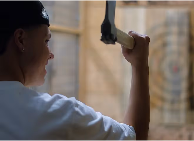A smiling young man preparing to throw an axe at a wooden target during a recreational activity at The Swiftwater Hotel.
