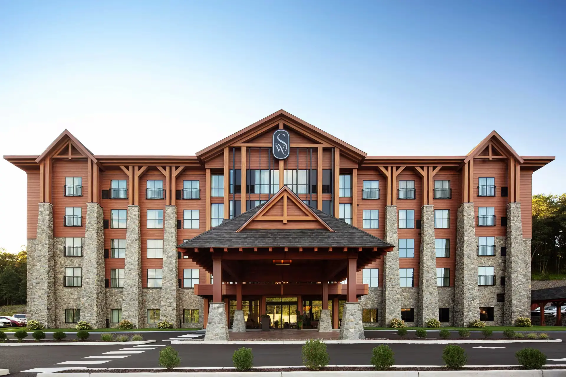 Panoramic view of The Swift Water hotel's grand lobby featuring high wood-paneled ceilings, a sparkling chandelier, stone walls, and a modern reception desk.