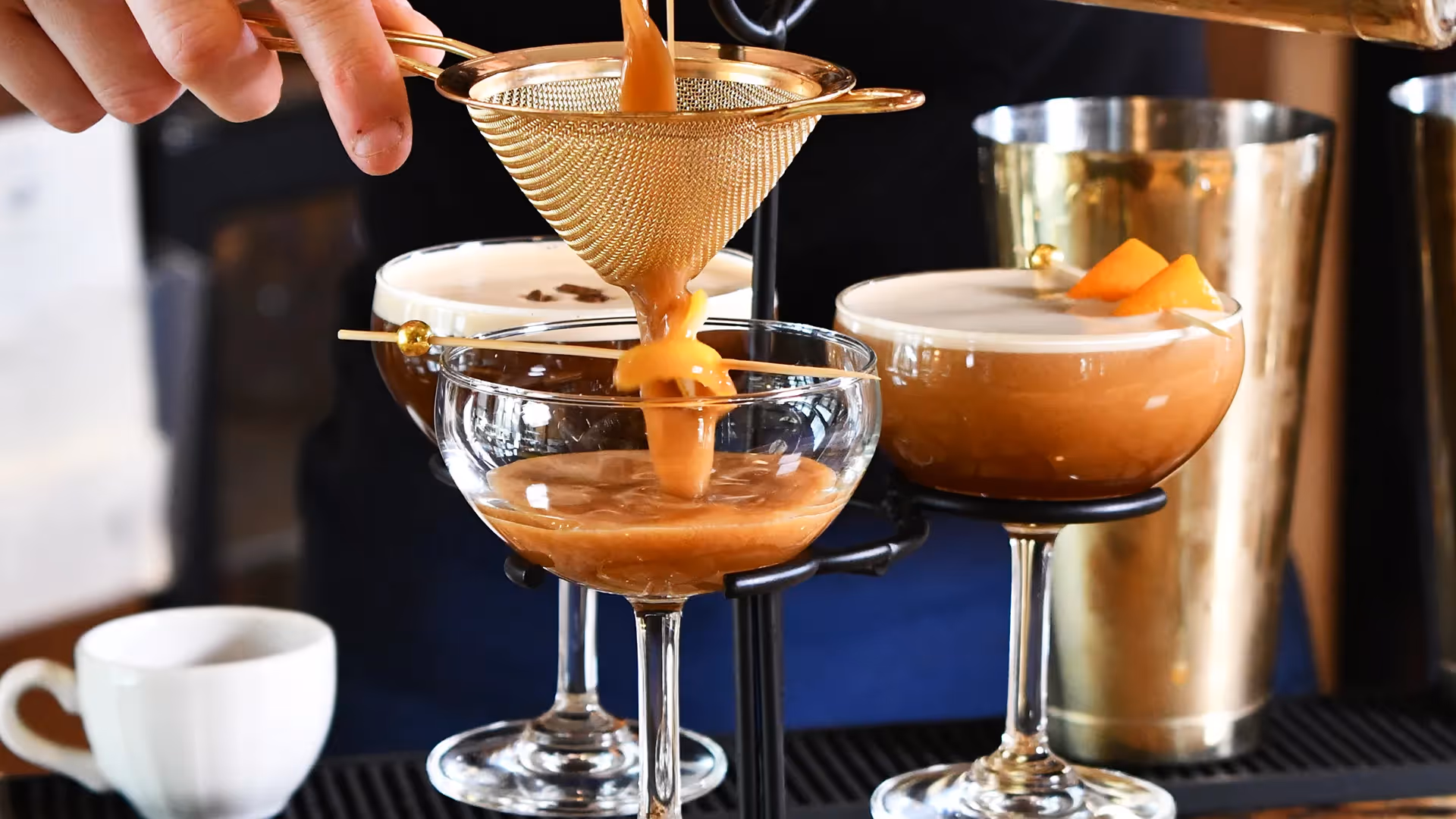 A bartender at The Swiftwater hotel meticulously double-straining a creamy espresso martini cocktail into elegant coupe glasses, showcasing luxury mixology and sophisticated drink service.