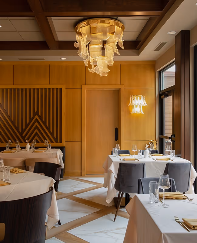 Elegant dining room at The Swiftwater hotel, featuring artistic chandeliers, geometric wood wall patterns, and sophisticated table settings for a premium fine dining experience.