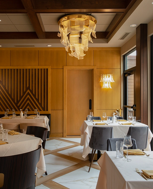 Elegant dining room at The Swiftwater hotel, featuring artistic chandeliers, geometric wood wall patterns, and sophisticated table settings for a premium fine dining experience.