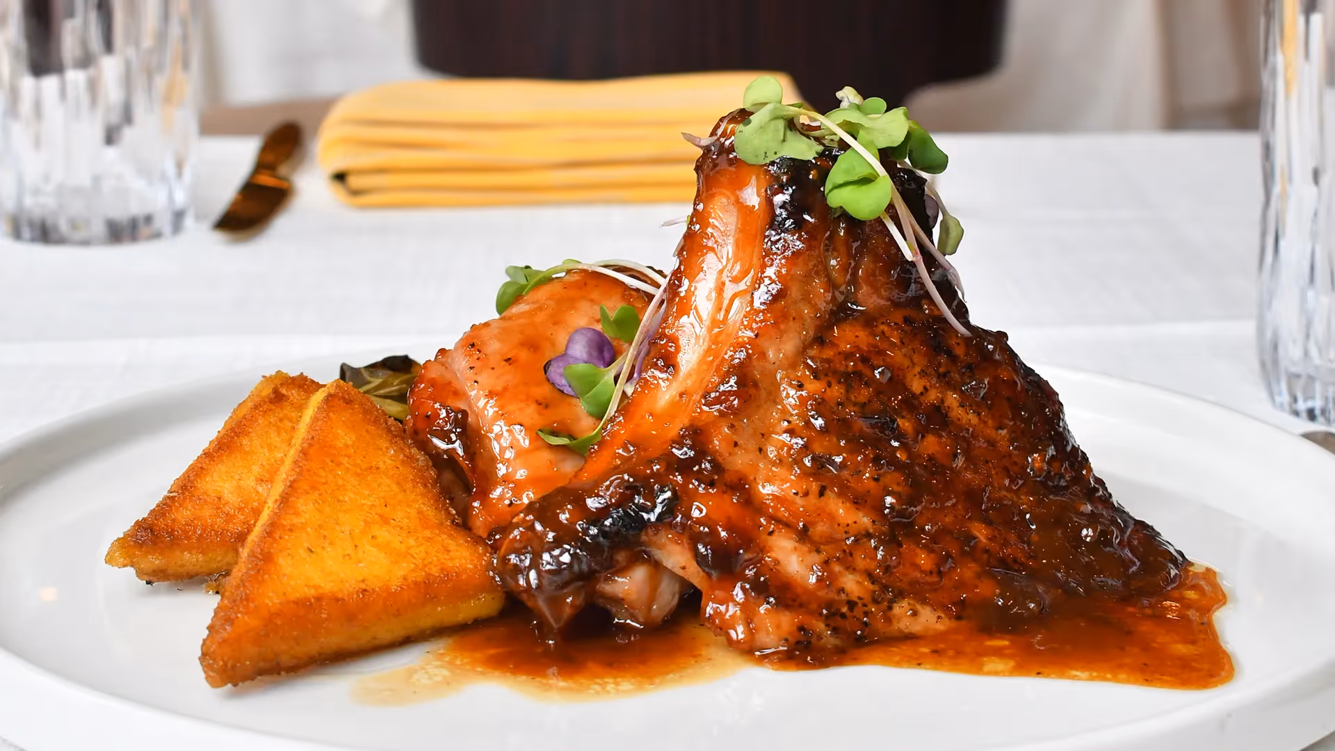 A succulent glazed pork chop served with crispy polenta triangles at The Swiftwater hotel restaurant, garnished with fresh microgreens for a gourmet dining experience.