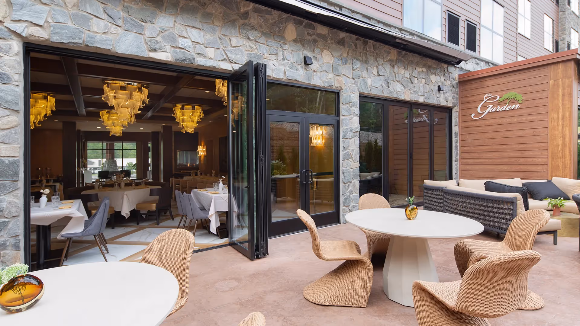 The Garden" outdoor terrace at The Swiftwater hotel, featuring stylish wicker furniture and an open-air dining area that seamlessly connects to the sophisticated interior restaurant.