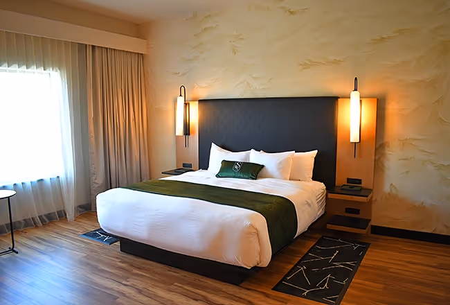 Luxury bedding at The Swiftwater hotel with emerald green runner, "SW" branded pillow, and designer bedside lamps.