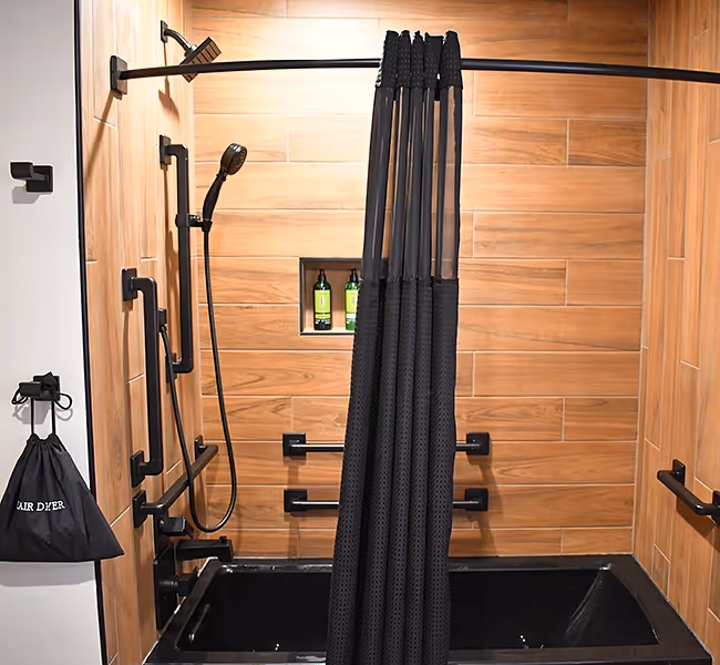 Luxurious shower space at The Swiftwater hotel featuring a deep black soaking tub, wood-look tiles, and accessible black grab bars.