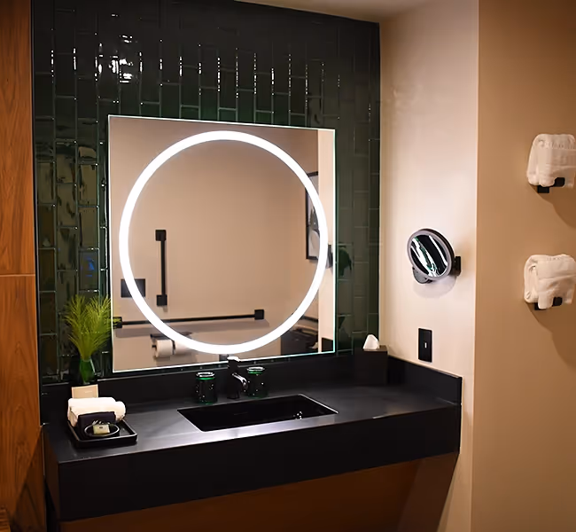 Sleek black vanity with a circular backlit mirror and green tile backsplash at The Swiftwater.