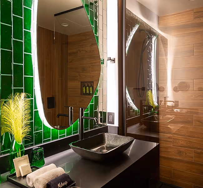Contemporary bathroom at The Swiftwater, boasting a bold emerald green tile backsplash, a unique backlit mirror, and a designer vessel sink on a black vanity.