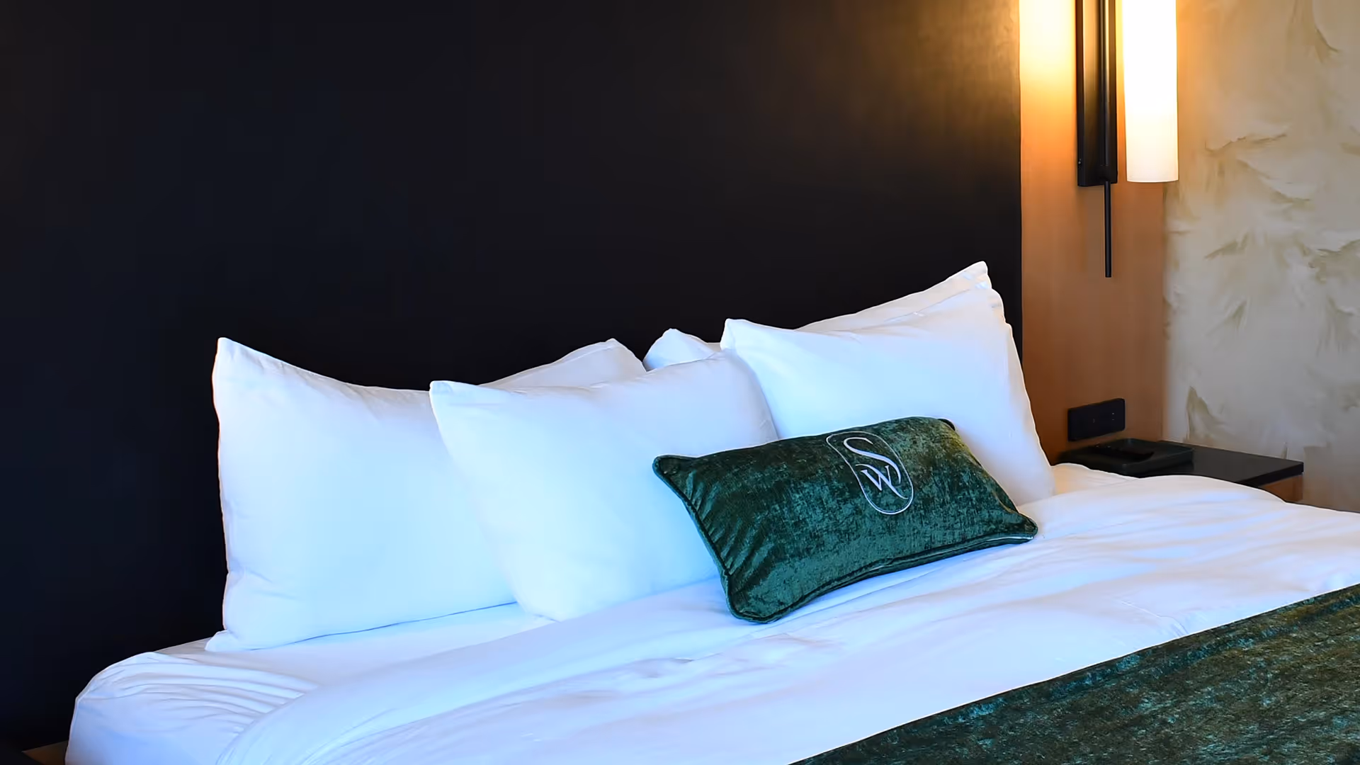 Luxury bedding at The Swiftwater hotel with emerald green runner, "SW" branded pillow, and designer bedside lamps.