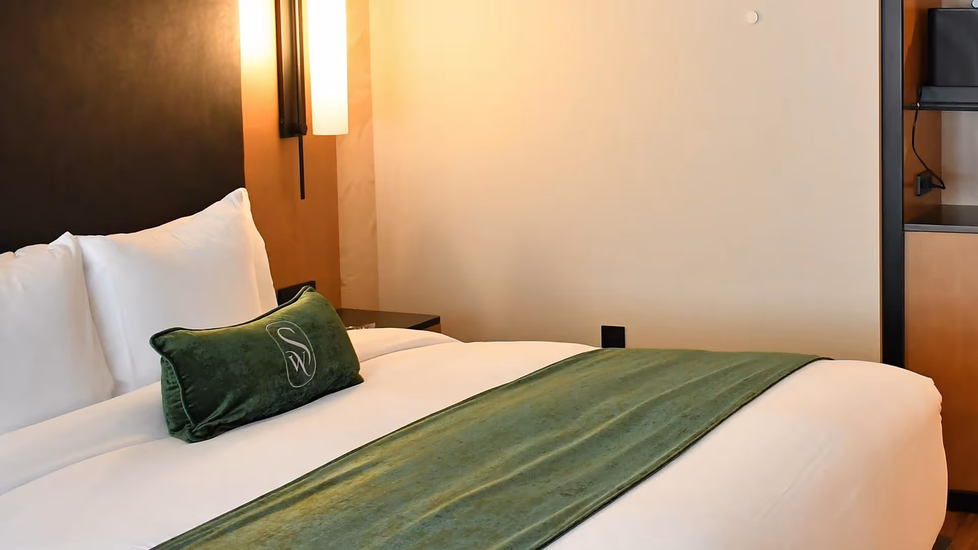 Detail of premium bedding at The Swiftwater hotel, featuring a forest green accent pillow and soothing warm lighting.