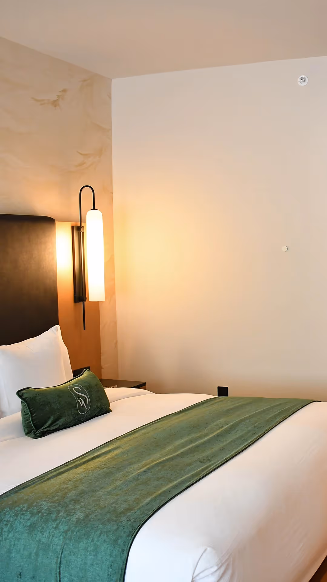 Detail of premium bedding at The Swiftwater hotel, featuring a forest green accent pillow and soothing warm lighting.