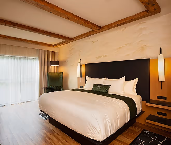 Bright luxury guest room at The Swiftwater hotel featuring a king bed, exposed wooden ceiling beams, and terrace access.