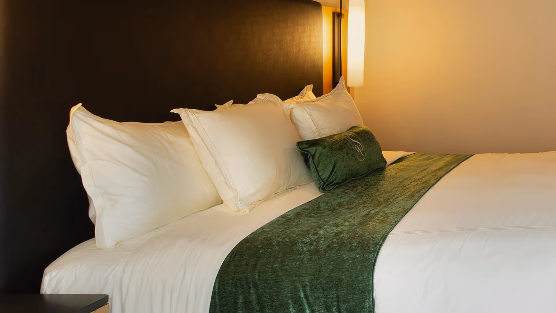 Close-up of premium bedding at The Swiftwater hotel featuring an emerald green bed runner and plush white pillows.