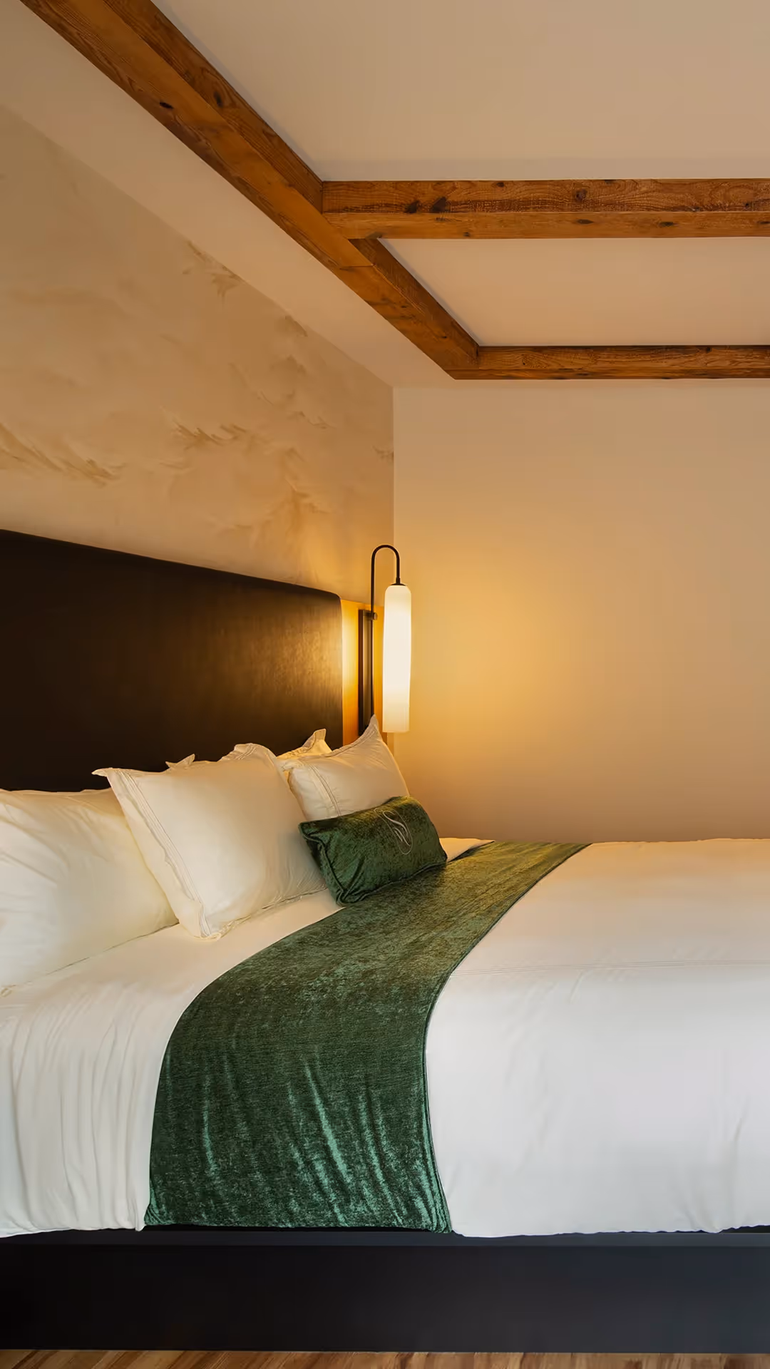 Close-up of premium bedding at The Swiftwater hotel featuring an emerald green bed runner and plush white pillows.