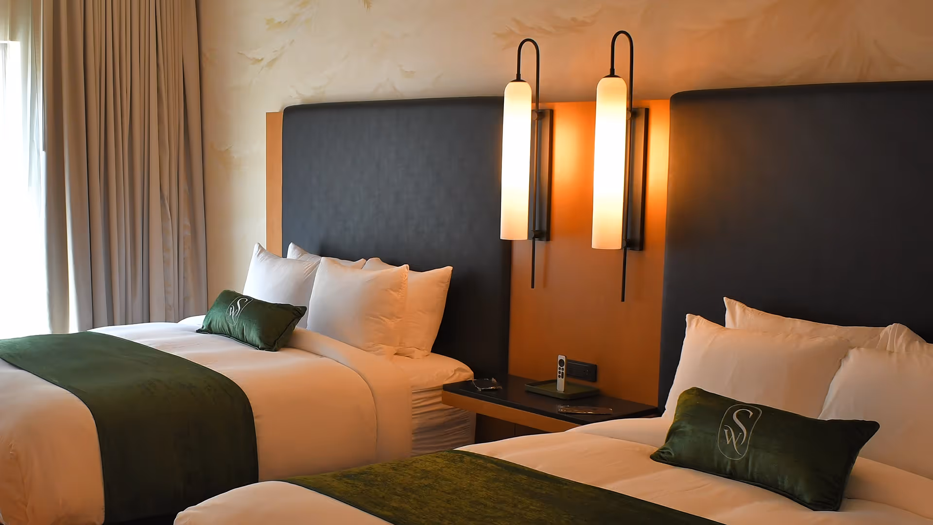 Guest room at The Swiftwater hotel featuring two beds, white linens, forest green accents, and warm lighting.