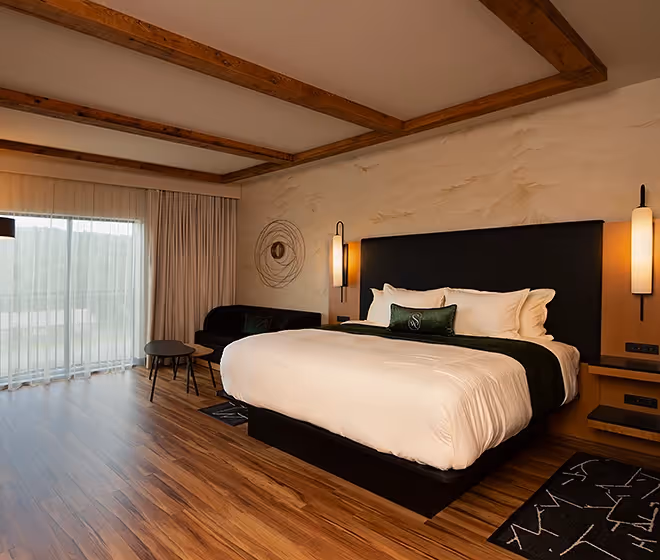 Luxurious living area at The Swiftwater hôtel featuring emerald green velvet armchairs, a modern crystal chandelier, and a wall-mounted screen displaying a pine forest, showcasing the hotel's elegant and cozy interior design.