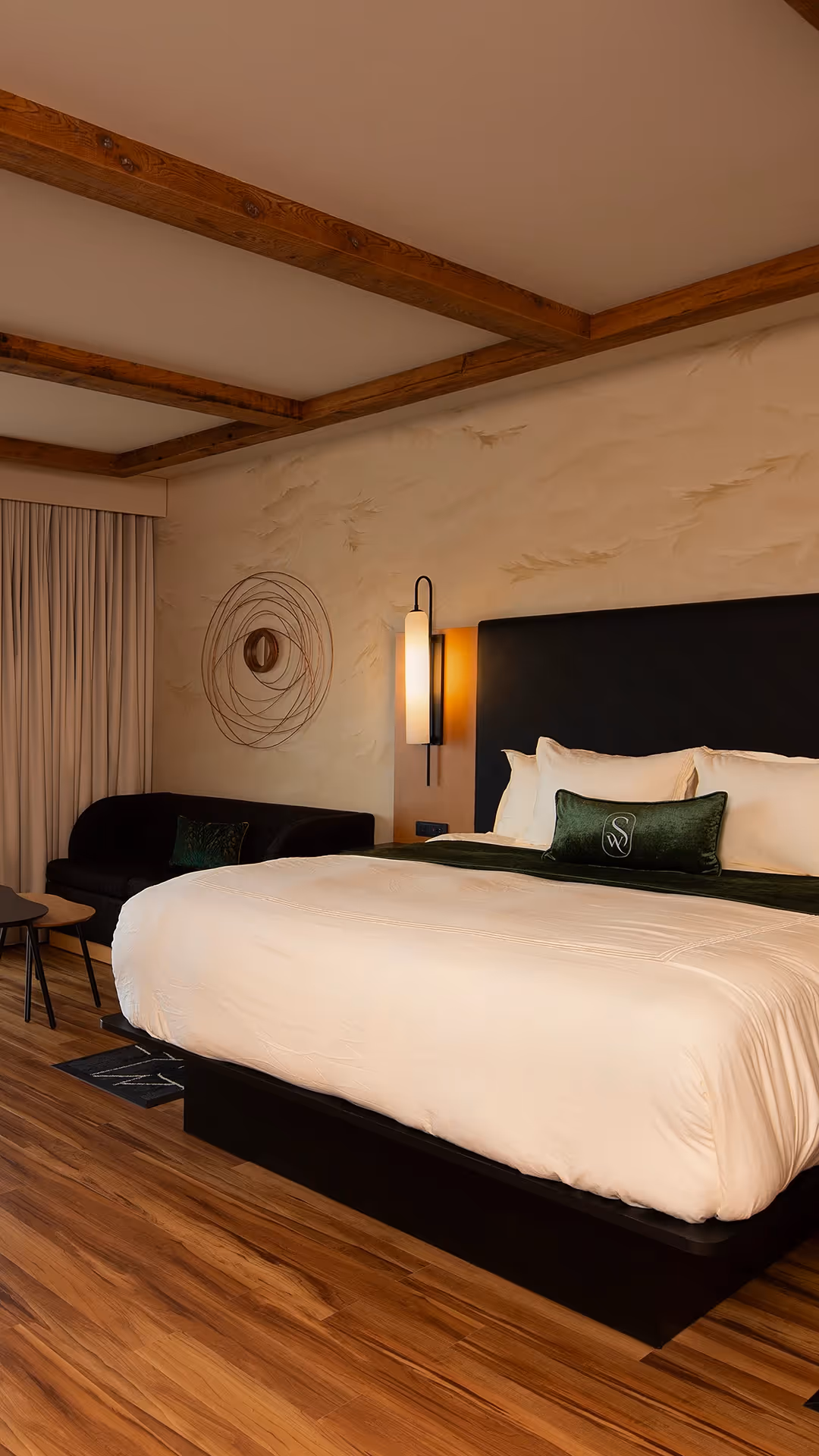 A welcoming close-up of the luxurious bed at The Swiftwater hotel, featuring plush white pillows, an emerald green accent throw, and a sleek dark headboard.