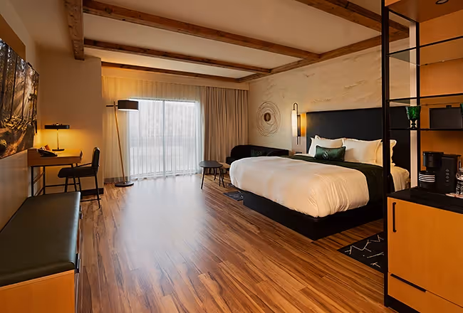 A stylish and bright guest room at The Swiftwater hotel, featuring a plush king-size bed, warm hardwood floors, and rustic ceiling beams.