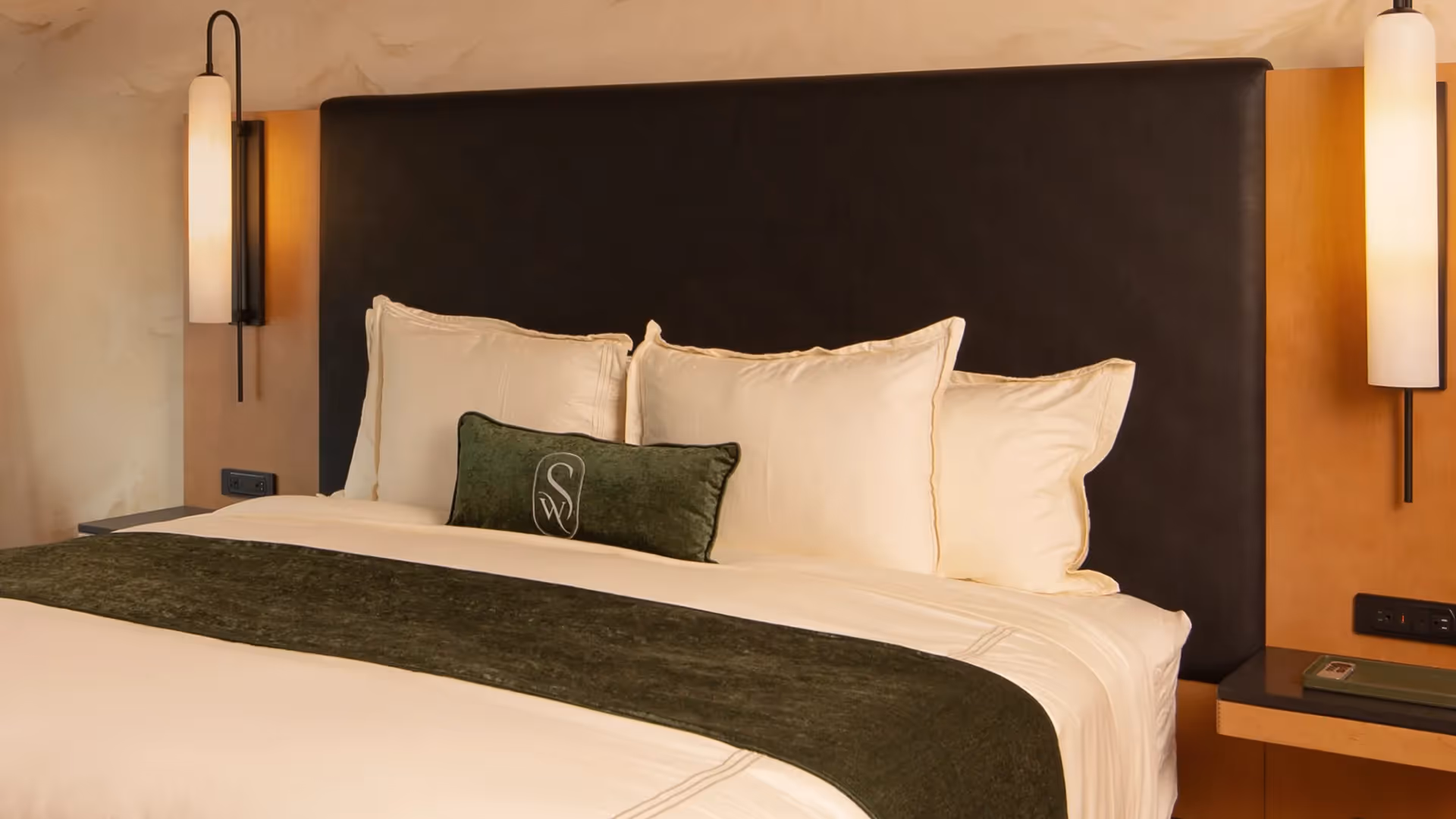 Close-up of the plush bedding at The Swiftwater with crisp white linens, forest green accent pillows, and sleek designer bedside lamps.