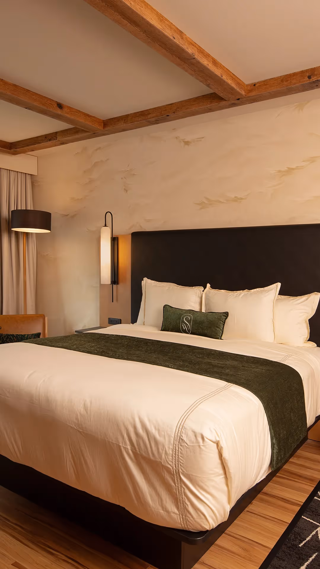 Close-up of the plush bedding at The Swiftwater with crisp white linens, forest green accent pillows, and sleek designer bedside lamps.