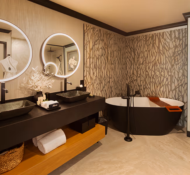 A modern bathroom at The Swiftwater hotel featuring a sleek black soaking tub, backlit circular mirrors, and chic mosaic tile decor.