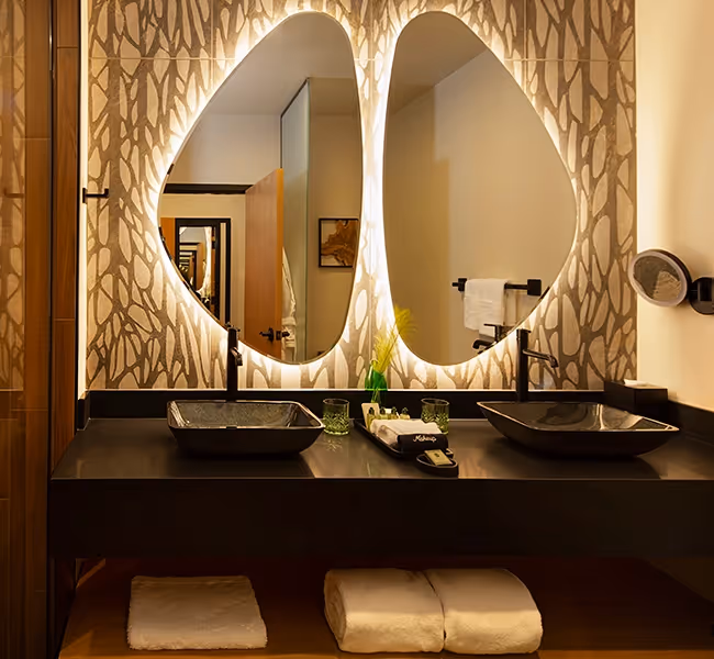 Modern bathroom vanity at The Swiftwater hotel featuring dual organically-shaped backlit mirrors, black vessel sinks, and natural wood finishesModern bathroom vanity at The Swiftwater hotel featuring dual organically-shaped backlit mirrors, black vessel sinks, and natural wood finishes